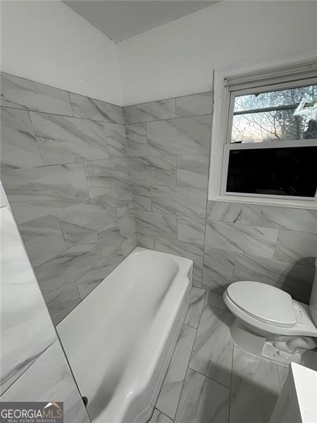 bathroom with a bath, tile walls, and toilet