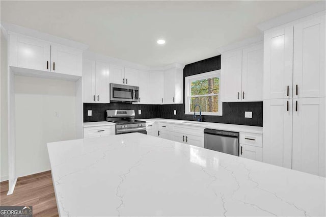 kitchen with white cabinets, light hardwood / wood-style floors, light stone counters, and stainless steel appliances