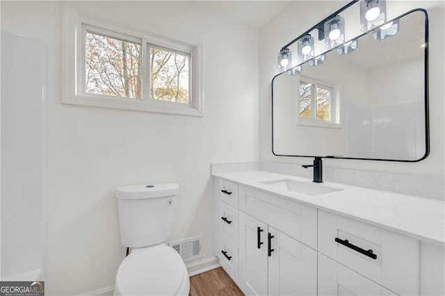 bathroom with wood-type flooring, vanity, toilet, and a healthy amount of sunlight