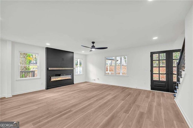 unfurnished living room with french doors, a large fireplace, light hardwood / wood-style flooring, and ceiling fan