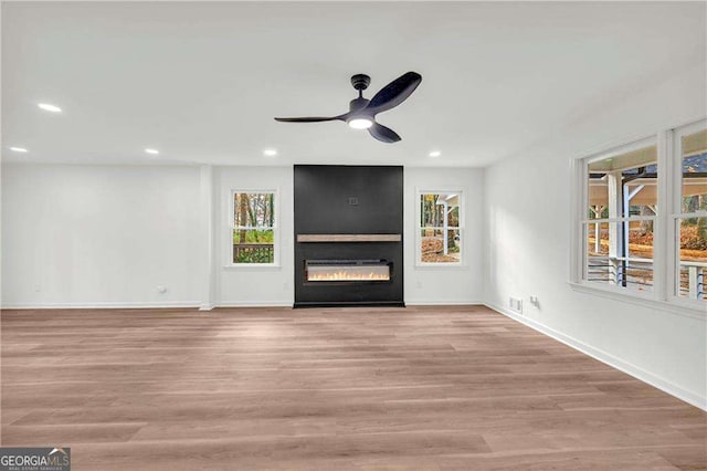 unfurnished living room with light wood-type flooring, a large fireplace, and a healthy amount of sunlight