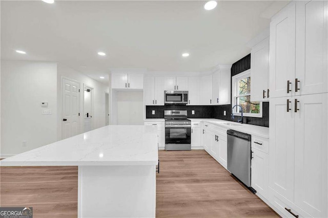 kitchen with white cabinets, a center island, light stone counters, and stainless steel appliances