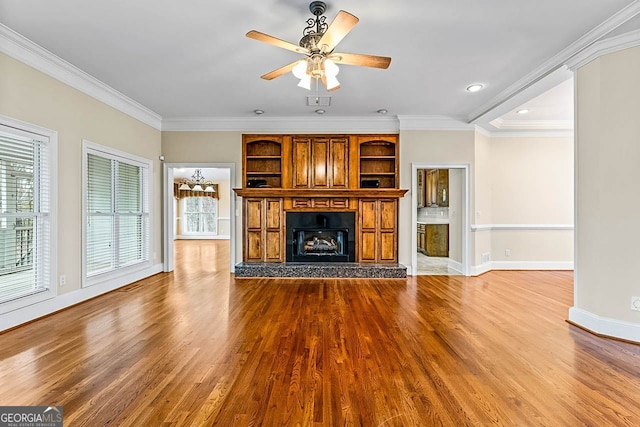 unfurnished living room featuring built in shelves, crown molding, ceiling fan, and light hardwood / wood-style floors