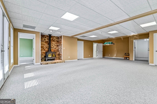 unfurnished living room featuring carpet flooring, a paneled ceiling, and a wood stove