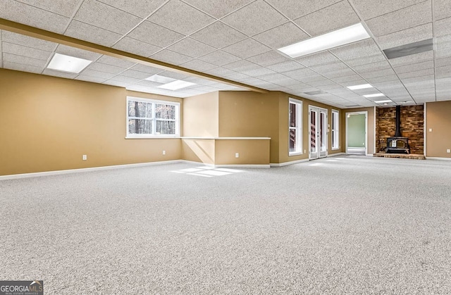 carpeted empty room featuring a paneled ceiling and a wood stove