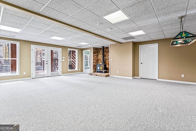 unfurnished living room with carpet, french doors, a paneled ceiling, and a wood stove