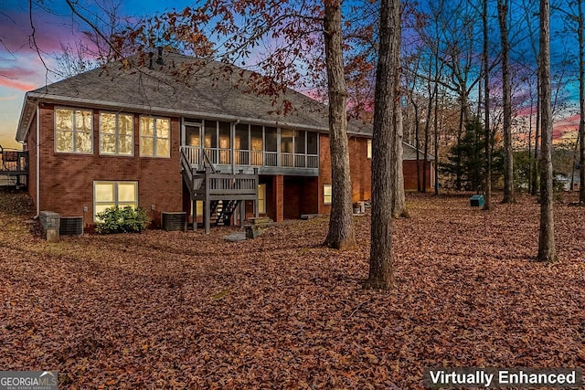 back house at dusk featuring central air condition unit and a sunroom