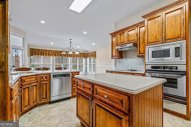 kitchen with sink, hanging light fixtures, decorative backsplash, a kitchen island, and stainless steel appliances