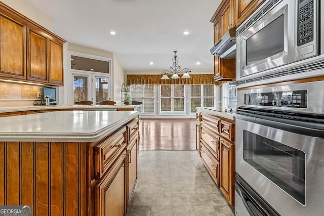 kitchen with appliances with stainless steel finishes, tasteful backsplash, light hardwood / wood-style flooring, and hanging light fixtures