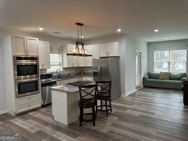 kitchen with appliances with stainless steel finishes, a breakfast bar, pendant lighting, stone counters, and a kitchen island