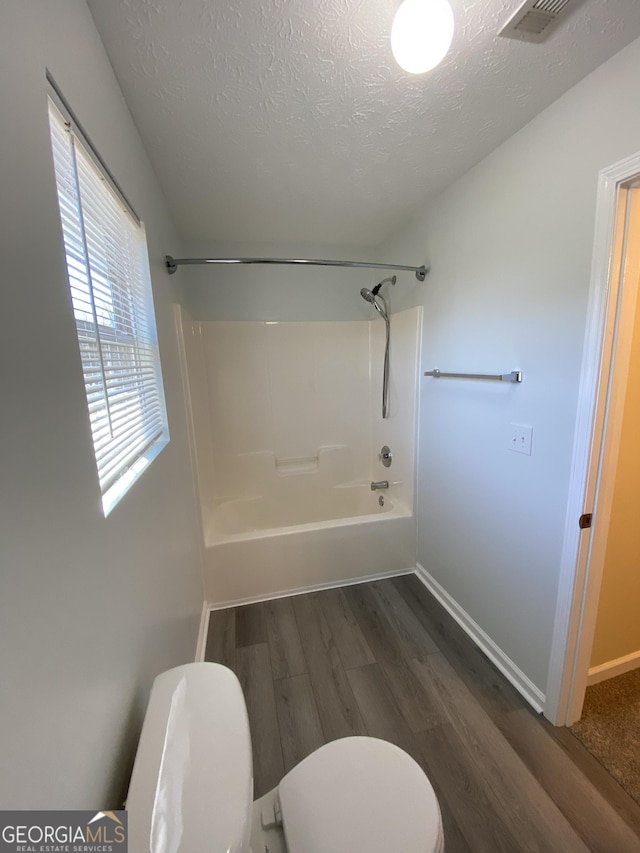 bathroom featuring hardwood / wood-style floors,  shower combination, toilet, and a textured ceiling