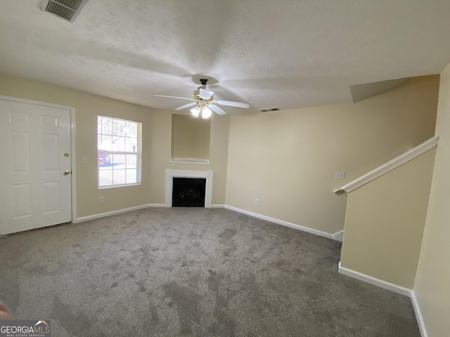 unfurnished living room with ceiling fan, dark carpet, and a textured ceiling