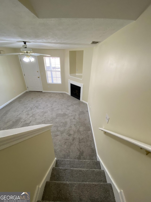 stairway featuring ceiling fan, carpet floors, and a textured ceiling