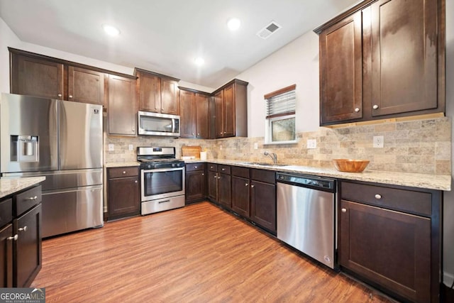 kitchen featuring light stone countertops, dark brown cabinetry, stainless steel appliances, sink, and light hardwood / wood-style floors