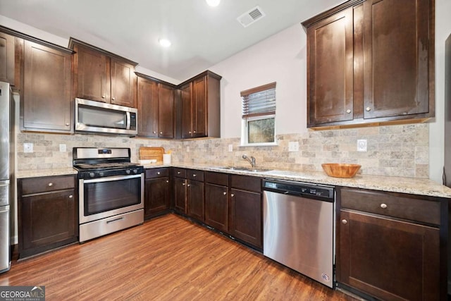 kitchen with sink, light stone counters, decorative backsplash, appliances with stainless steel finishes, and light wood-type flooring