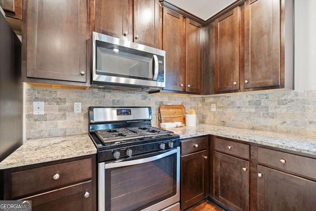 kitchen featuring light stone countertops, appliances with stainless steel finishes, dark brown cabinetry, and tasteful backsplash