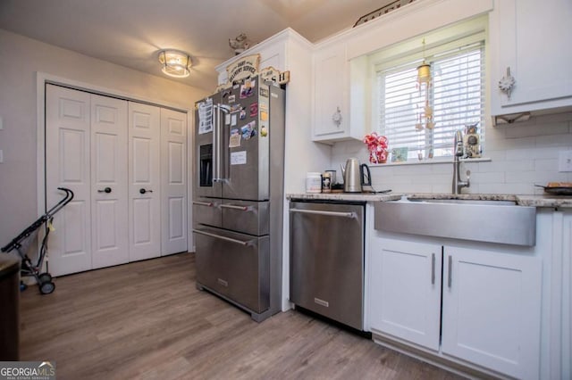 kitchen with backsplash, sink, light hardwood / wood-style flooring, white cabinetry, and stainless steel appliances