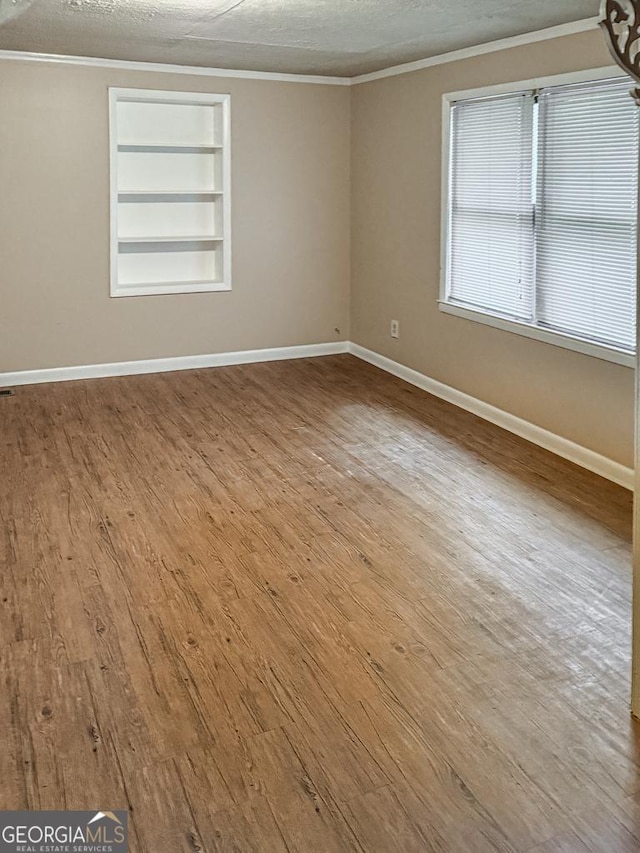 empty room with built in features, crown molding, a textured ceiling, and light hardwood / wood-style flooring