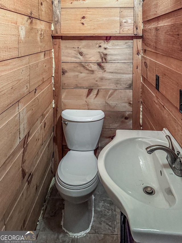 bathroom featuring toilet, sink, and wooden walls