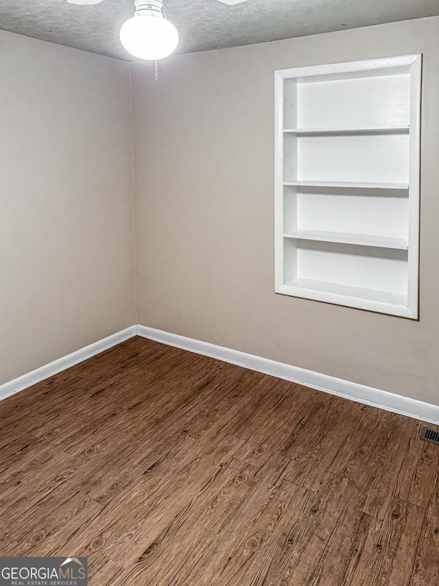 empty room featuring a textured ceiling, wood-type flooring, and built in shelves