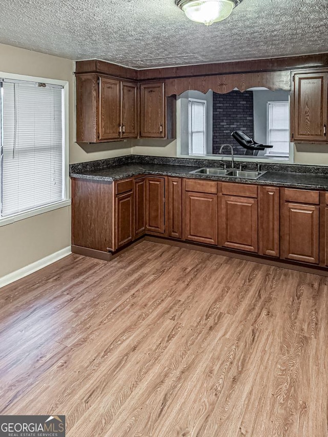 kitchen with light hardwood / wood-style floors, sink, a textured ceiling, and dark stone counters