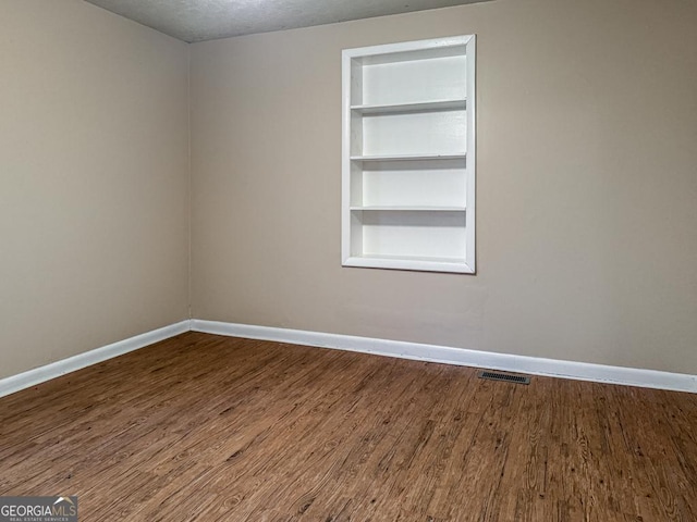 spare room with a textured ceiling, built in features, and hardwood / wood-style flooring