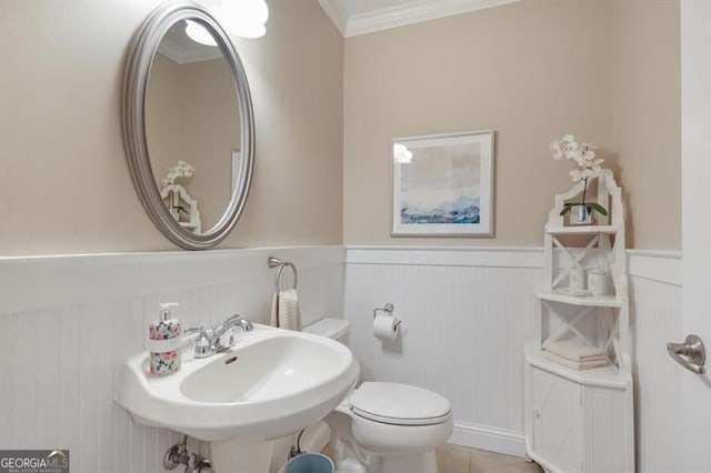 bathroom featuring toilet, a wainscoted wall, ornamental molding, tile patterned flooring, and a sink