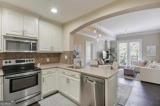 kitchen with kitchen peninsula, light wood-type flooring, stainless steel appliances, decorative light fixtures, and white cabinetry