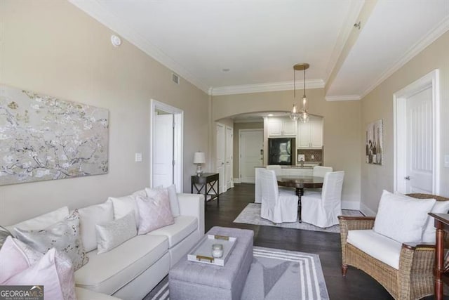 living area featuring arched walkways, dark wood-style flooring, visible vents, baseboards, and ornamental molding