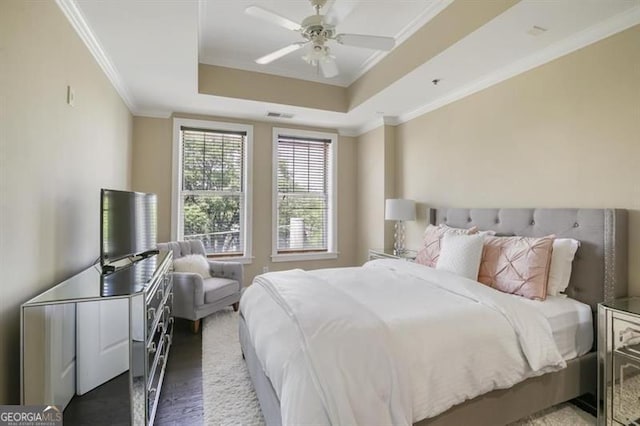 bedroom with dark hardwood / wood-style floors, ceiling fan, crown molding, and a tray ceiling