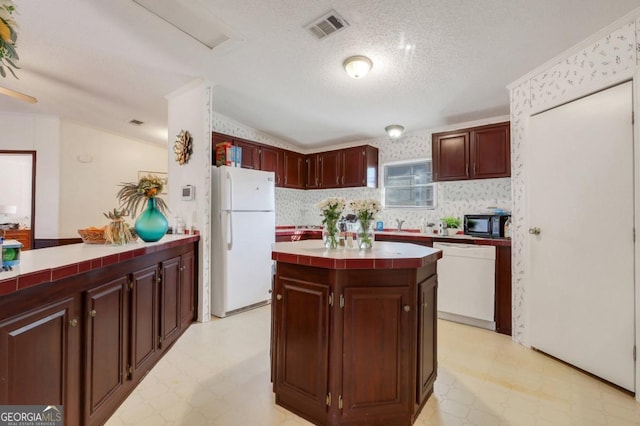 kitchen with a center island, white appliances, vaulted ceiling, a textured ceiling, and tile counters