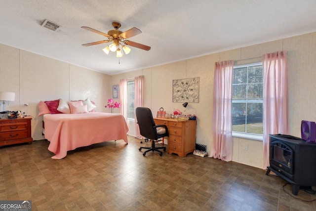 bedroom with multiple windows, a textured ceiling, a wood stove, and ceiling fan