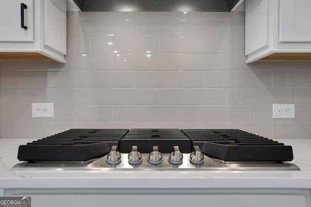 details with decorative backsplash, stainless steel gas cooktop, wall chimney range hood, white cabinetry, and light stone counters