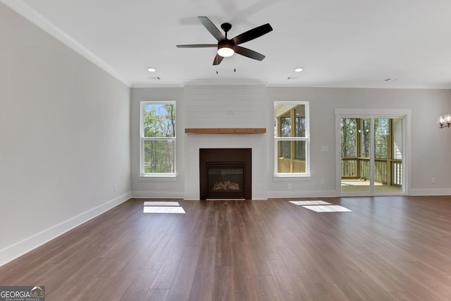 unfurnished living room featuring a large fireplace, wood finished floors, baseboards, ceiling fan with notable chandelier, and ornamental molding
