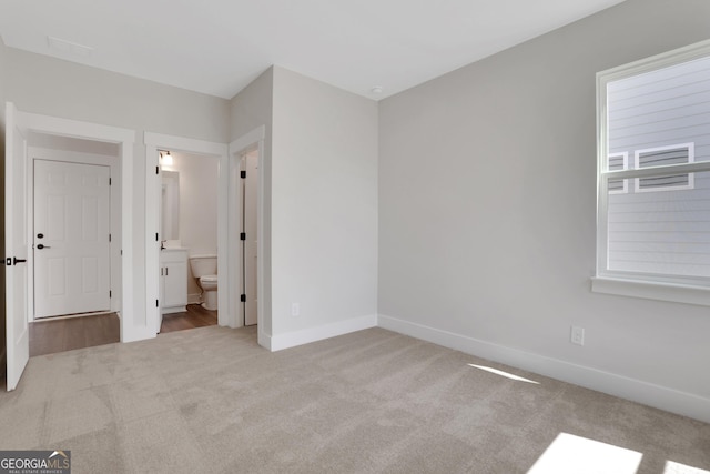 unfurnished bedroom with baseboards, ensuite bathroom, and carpet