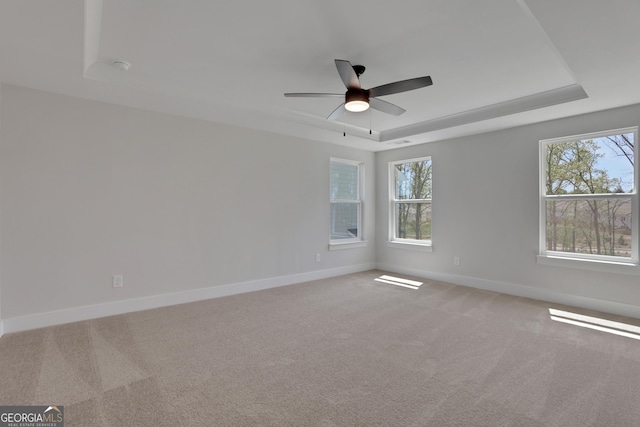 spare room featuring a ceiling fan, a tray ceiling, light carpet, and baseboards