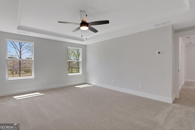 empty room featuring ceiling fan, light carpet, a raised ceiling, baseboards, and visible vents