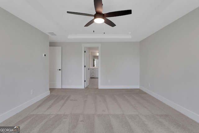 unfurnished bedroom with visible vents, baseboards, light colored carpet, a raised ceiling, and ensuite bath