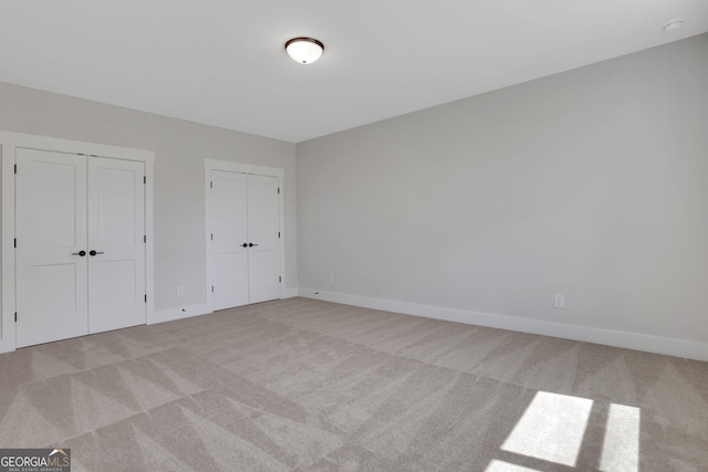 unfurnished bedroom featuring baseboards, multiple closets, and light carpet