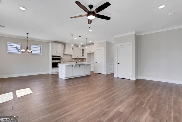 unfurnished living room featuring recessed lighting, baseboards, ornamental molding, and ceiling fan with notable chandelier