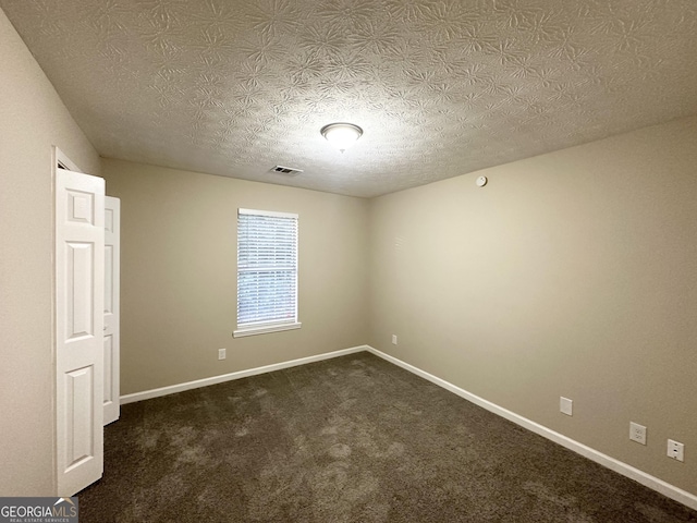 empty room featuring dark colored carpet and a textured ceiling