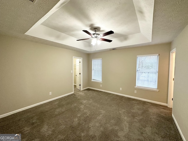 carpeted empty room with a raised ceiling, ceiling fan, a healthy amount of sunlight, and a textured ceiling