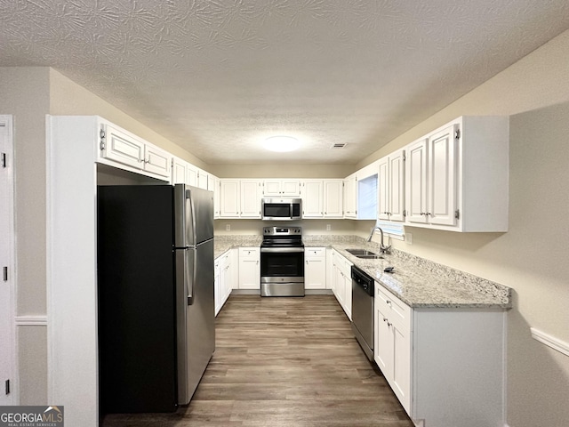 kitchen with light stone countertops, sink, dark wood-type flooring, white cabinets, and appliances with stainless steel finishes