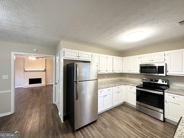 kitchen featuring dark wood-type flooring, white cabinets, a brick fireplace, light stone countertops, and appliances with stainless steel finishes