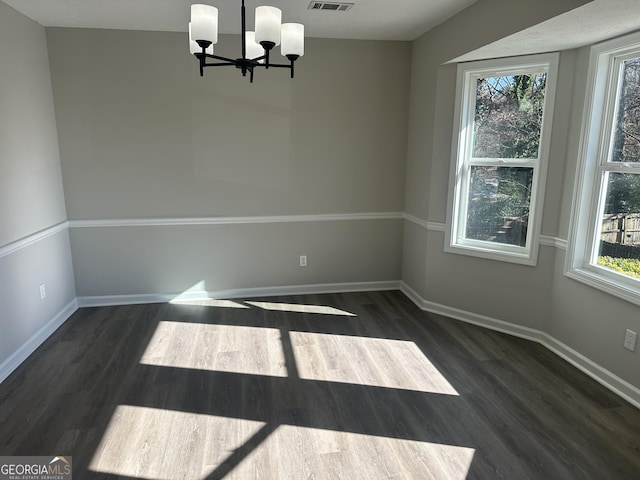 empty room featuring dark hardwood / wood-style floors, an inviting chandelier, and a wealth of natural light