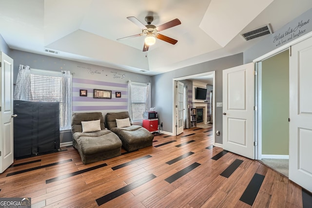 interior space featuring a raised ceiling, a fireplace, ceiling fan, and hardwood / wood-style floors