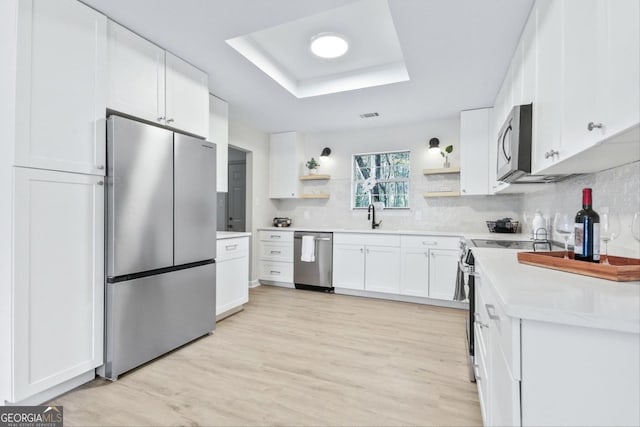 kitchen with tasteful backsplash, appliances with stainless steel finishes, white cabinetry, a raised ceiling, and open shelves