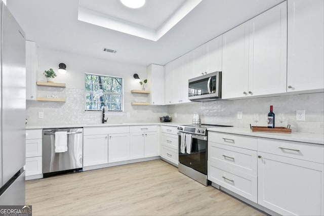 kitchen with a sink, open shelves, a tray ceiling, and stainless steel appliances