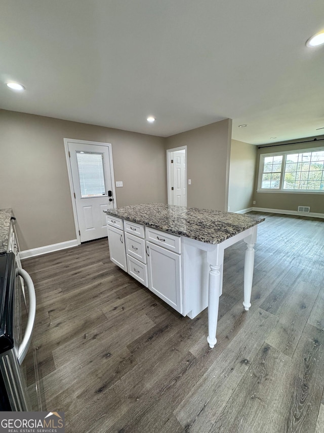 kitchen with dark hardwood / wood-style flooring, a breakfast bar, stone countertops, white cabinets, and a kitchen island