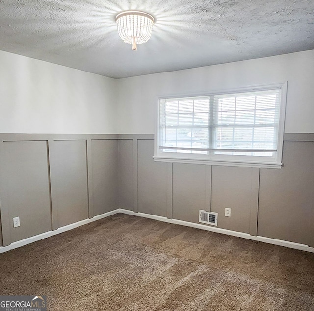 carpeted empty room with a chandelier and a textured ceiling